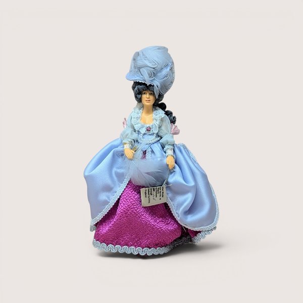 A vintage Peggy Nisbet costume doll in a black and white striped gown with ruffles, centered on a beige background.