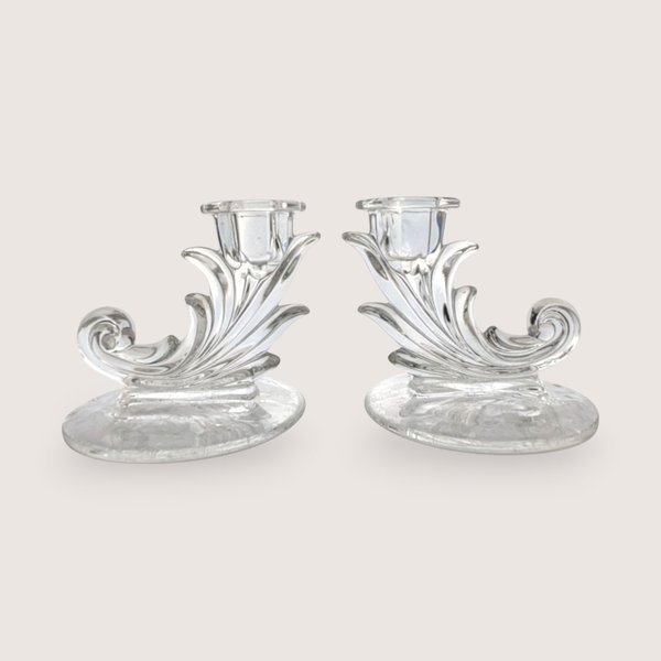 A pair of vintage clear glass cornucopia or leaf-shaped single candlestick holders, centered on a beige background.