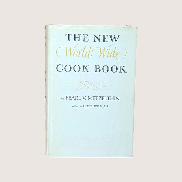 Vintage cookbook titled The New World Wide Cook Book by Pearl V Metzelthin centered on a plain linen background.