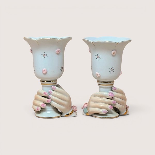 Pair of white porcelain hand vases with pink floral details and gold trim, centered on a plain linen background.