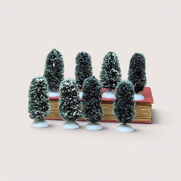 Set of eight small vintage Department 56 frosted bottle brush topiary trees lined up in front of an old book.