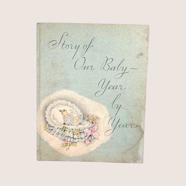 A vintage 1934 Story of Our Baby record book featuring a bassinet illustration on a light blue cover.