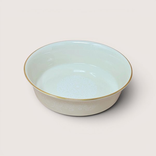 Round ceramic serving bowl with a white floral medallion design on the interior and a gold rim, centered on a plain linen background.
