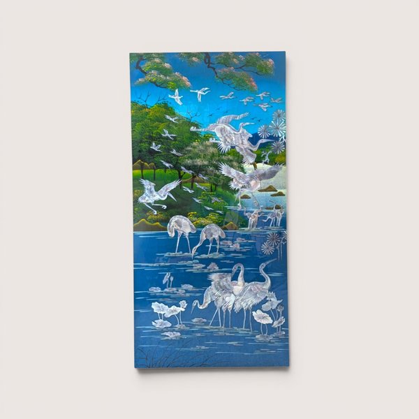 A vintage Asian wall panel featuring a blue landscape scene with detailed iridescent mother of pearl inlaid cranes.