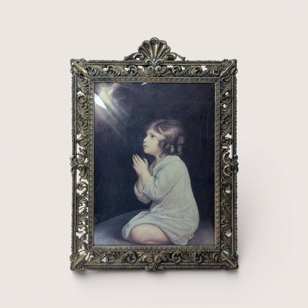 A vintage heavy ornate brass frame holding Sir Joshua Reynolds painting of The Infant Samuel behind curved bubble glass.