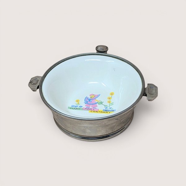Vintage metal child's warming bowl with an enamel interior featuring a central "Mary Mary Quite Contrary" nursery rhyme illustration, centered on a plain linen background.