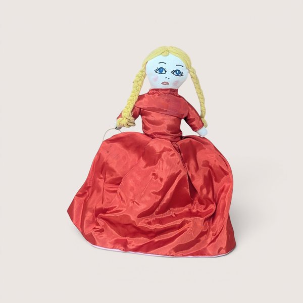 Handmade cloth doll with yellow yarn braids wearing a voluminous red satin gown, centered on a plain linen background.
