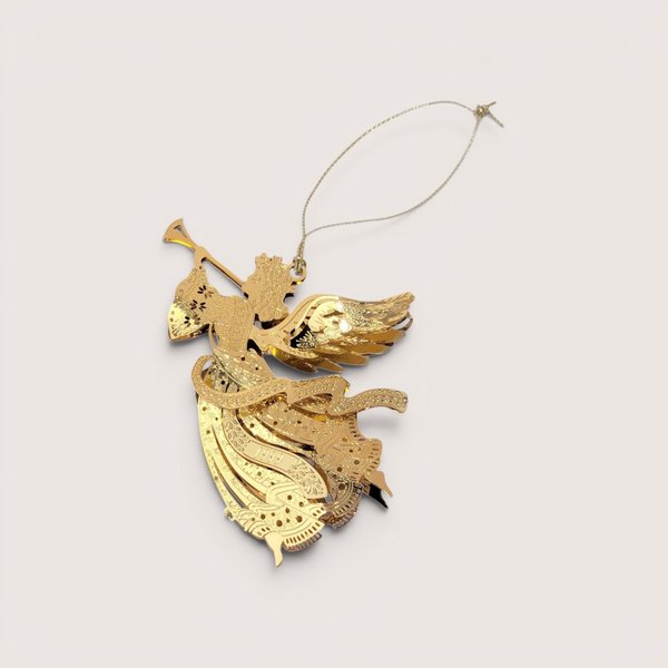 A 1999 Danbury Mint Millennium Angel Christmas ornament with its box on a soft pink background. The fine filigree brass angel is plated in gleaming 23kt gold, depicted in flight while blowing a long trumpet with a dated 1999 banner ribbon.