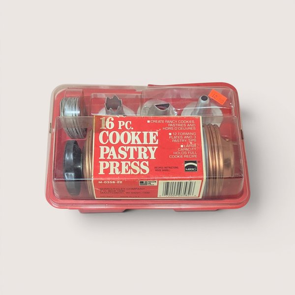 A vintage 16 piece Mirro cookie and pastry press kit in its original red and clear plastic storage case.