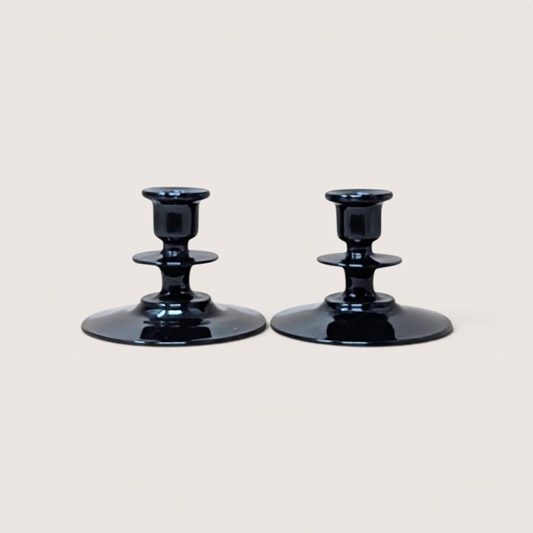 A pair of vintage black glass candle holders with tiered stems and wide round bases on a plain background