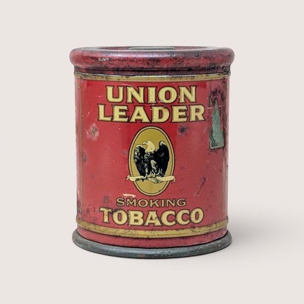 A vintage red Union Leader Smoking Tobacco cylindrical tin with an eagle emblem on a plain background