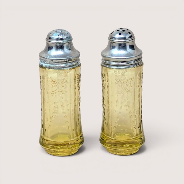 A pair of amber depression glass salt and pepper shakers with silver metal lids on a plain beige background