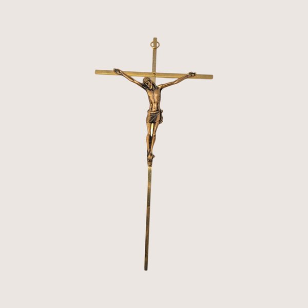 A slim vintage brass colored crucifix wall hanging featuring a detailed bronze tone corpus on a light cream background