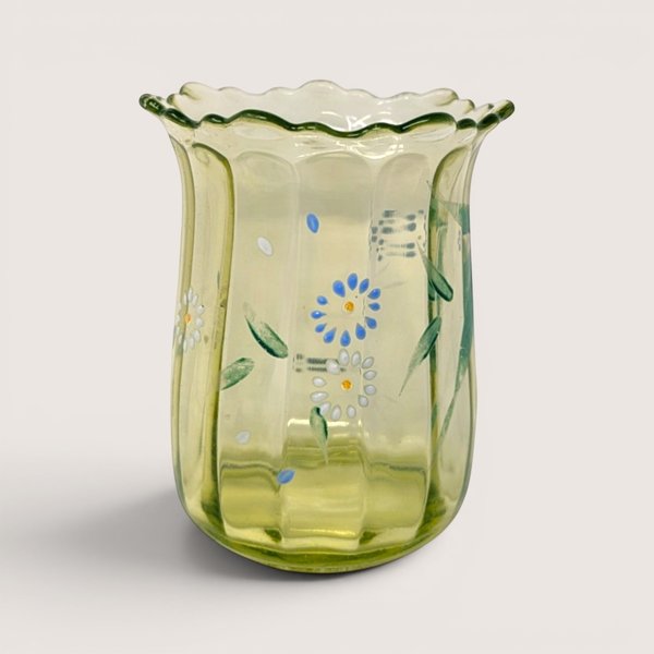 Antique light green glass vase with hand-painted blue and white flowers and a ruffled rim against a solid cream background.