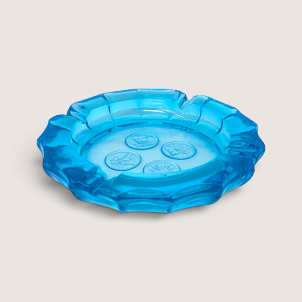 Vintage round bright blue Fostoria glass ashtray featuring four frosted coin designs embossed in the center.
