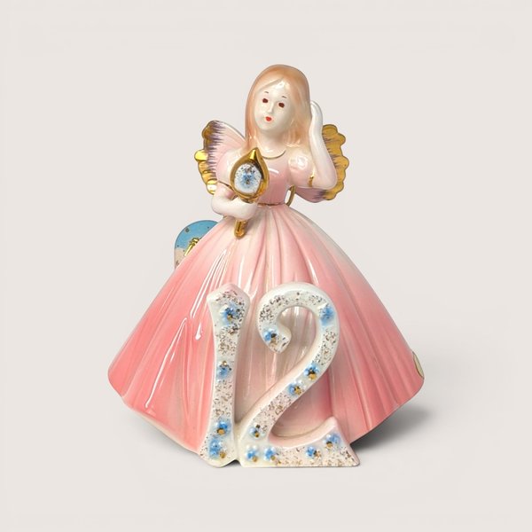 Vintage Josef Originals age 12 birthday girl porcelain figurine holding a gold hand mirror on a linen background.