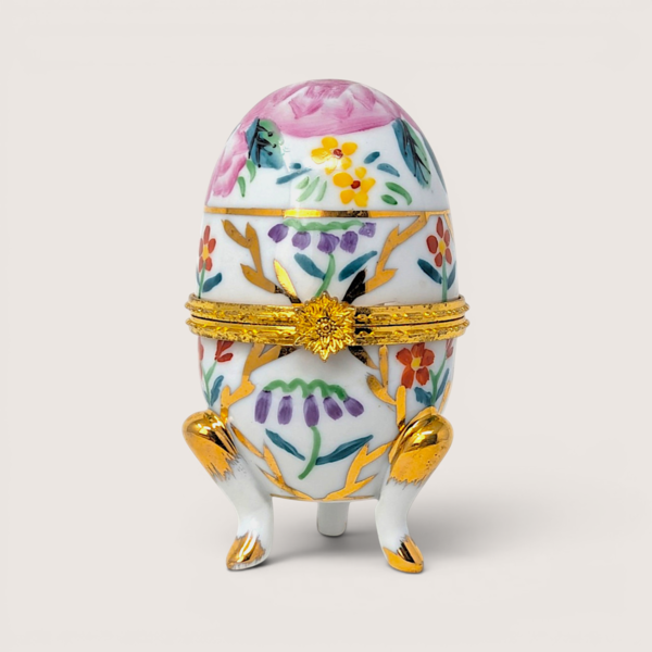 Hand painted white porcelain footed egg trinket box with colorful flowers, gold scrollwork, and a flower clasp.