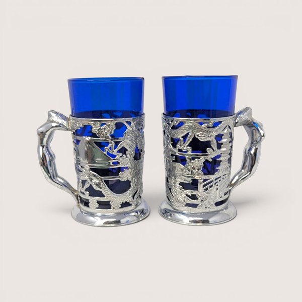 Pair of vintage Japanese silver-plated tankards with cobalt blue glass liners and detailed figural handles.
