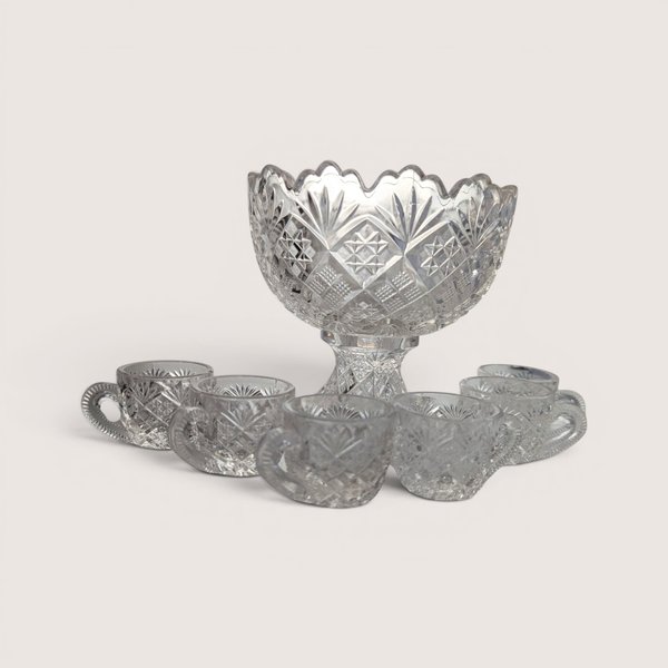Vintage miniature cut glass punch bowl on a pedestal stand surrounded by six small glass cups.