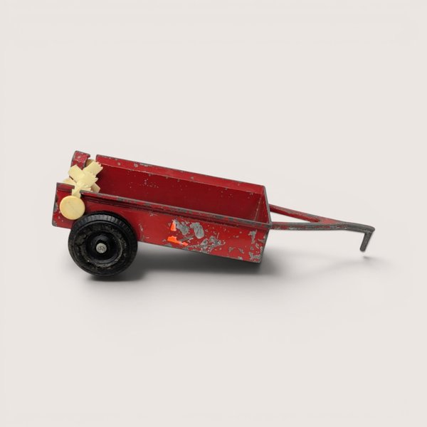 Vintage red ERTL diecast manure spreader farm trailer toy with heavy paint chipping against a light backdrop.