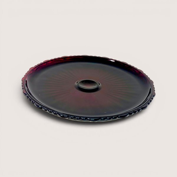 Vintage 1970s Avon Cape Cod ruby red pressed glass pie plate showing a detailed geometric rosette pattern from above.