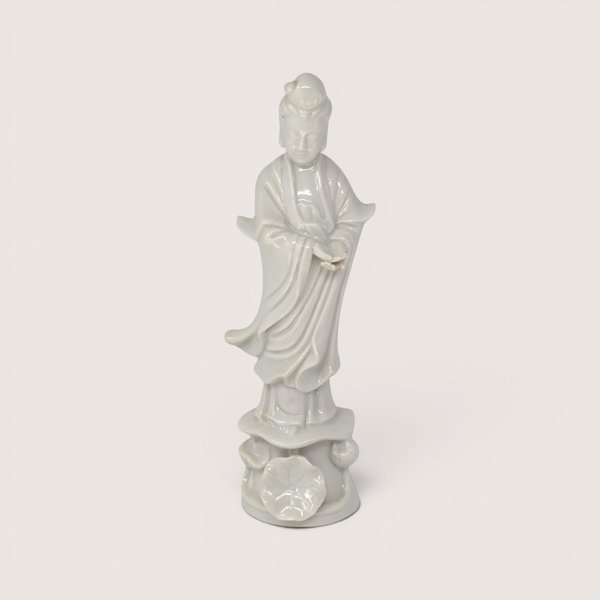 Vintage white porcelain Guan Yin statue standing on a sculpted lotus leaf pedestal base against a light background.
