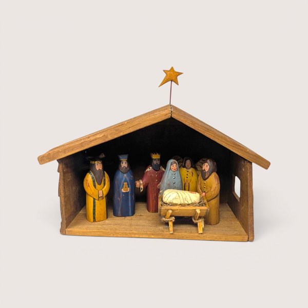 Vintage handmade wooden nativity set featuring a stable manger with a star and hand-carved painted figures inside.