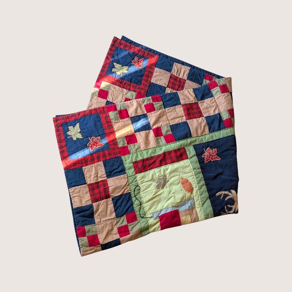 Vintage 1990s handmade patchwork cabin quilt featuring plaid blocks, applique leaves, a tiny house, and a deer.
