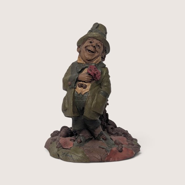 Vintage 1980s Tom Clark Cairn Studios gnome figurine holding a red rose and standing on a base of autumn leaves and acorns.