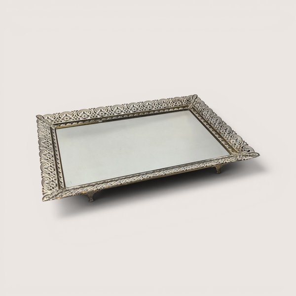 Vintage ornate filigree vanity mirror tray with a detailed metal border set against a plain linen background.
