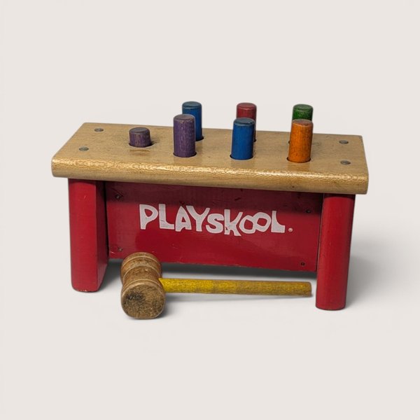 Vintage wooden Playskool pounding bench with colored pegs and a matching mallet on a light background.