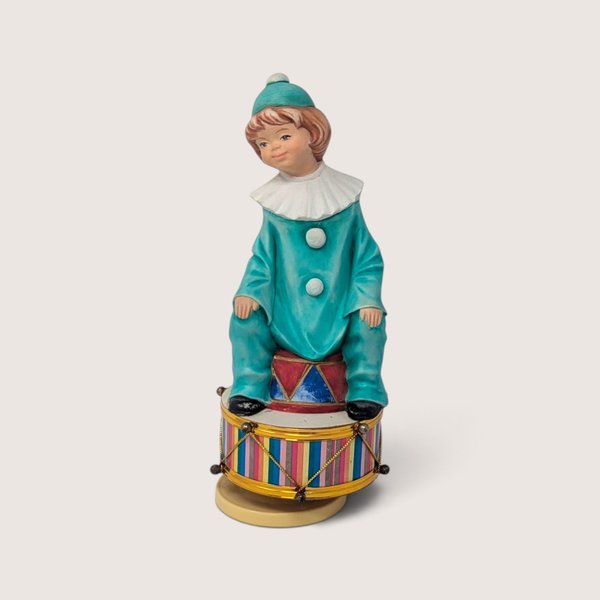 Vintage ceramic rotating music box featuring a clown in a teal outfit sitting on a colorful striped drum.