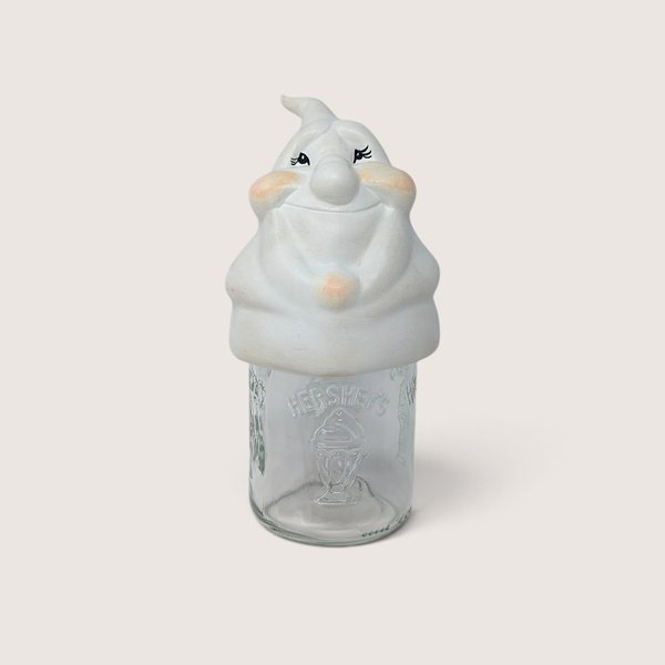 Vintage ceramic ghost mason jar topper with painted rosy cheeks sitting on a clear Hershey glass jar.