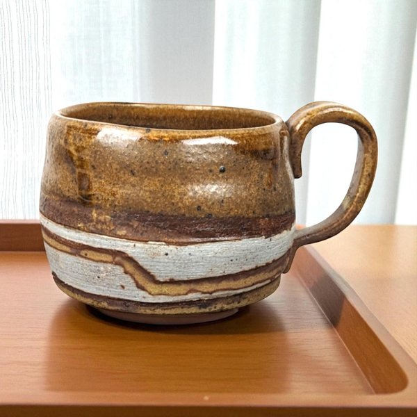 A 2.75-inch tall handcrafted brown stoneware mug with a wide, rounded body featuring horizontal white, dark brown, and light gray geometric bands and a rustic flared rim.