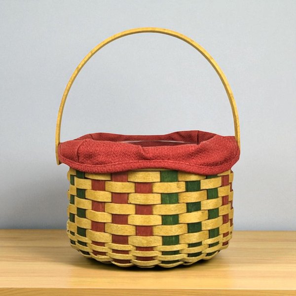A round, hand-woven maple wood basket with a single swinging handle, featuring a festive red and green accent weave and a red fabric liner.