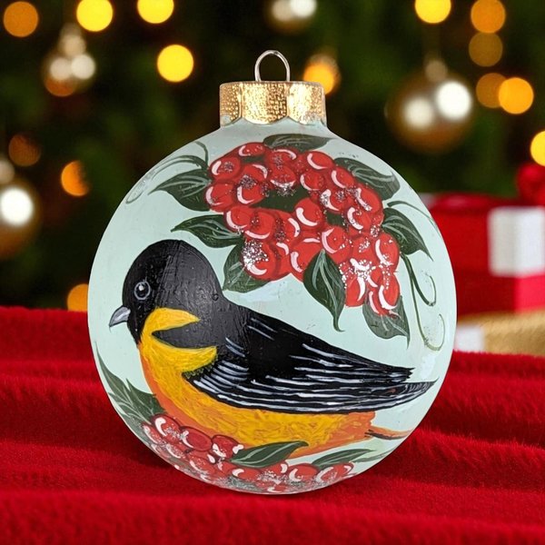 A 4-inch round glass Christmas ornament with a hand-painted yellow and black bird perched among clusters of bright red berries on a pale mint green background.
