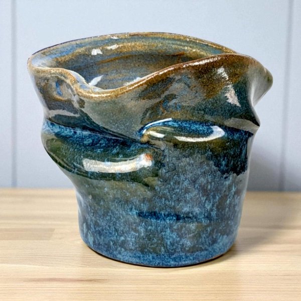 A 5-inch tall blue glazed ceramic vase with an asymmetrical, folded rim and a textured "crushed" body.