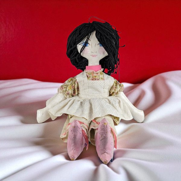 A large 25-inch handmade doll with a hand-painted paper mache head, hands, and feet, featuring black yarn hair, blue eyes, and wearing a floral dress with a white eyelet pinafore.