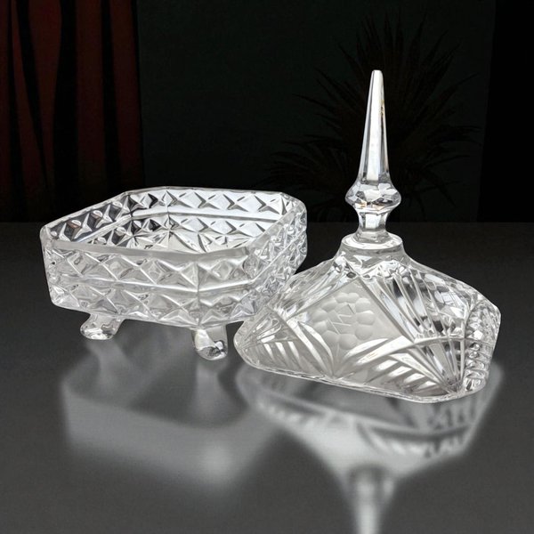 A clear pressed glass square trinket box with four scrolled feet. The base features a diamond quilted texture, while the matching lid is topped with a tall, faceted spire finial. Light reflects through the sharp, geometric cuts of the glass.