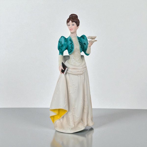 Two hand-painted matte porcelain figurines of women in Victorian attire. One wears a pink floral gown with a black hat and stands with suitcases; the other wears a cream lace gown with a teal bolero jacket, holding a teacup and a book.