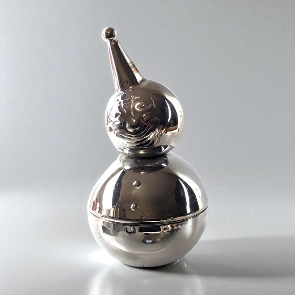 A vintage silver-toned metal clown bank with a rounded, weighted base, featuring a smiling face, a pointed hat, and two buttons on the front.