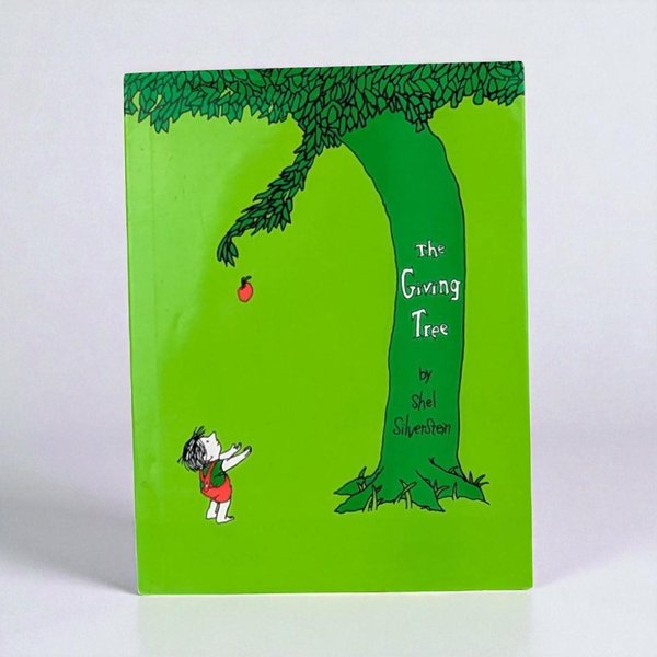 The cover of the hardcover book The Giving Tree features a vibrant green background with a minimalist black line drawing of a tall tree. A small child in red overalls reaches up toward a single red apple falling from a branch.
