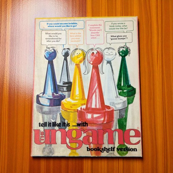 Vintage board game box for The Ungame Bookshelf Version featuring stylized, colorful game pawns with illustrated faces. The primary colors include bold red, yellow, green, and blue figures set against a cream background with conversational prompt bubbles.