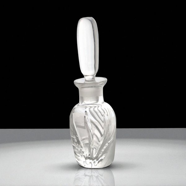 A small, clear glass perfume bottle with a heavy, rounded base featuring deep vertical and swirling carved grooves. It is topped with a tall, smooth, oblong glass stopper that has a frosted neck for a secure fit.