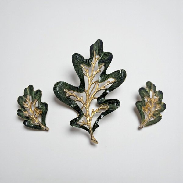A set of gold-tone oak leaf jewelry including a large brooch and two matching earrings. The pieces feature deep forest green enamel with a textured, ribbed finish and polished gold-tone veining that mimics a skeletal leaf structure.