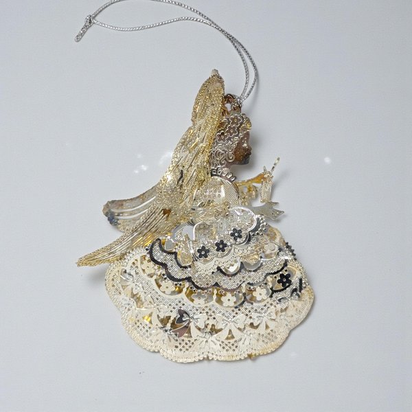 Silver plated metal ornament of a praying angel with large feathered wings and a long flowing gown. The surface has a soft aged patina with visible tarnish in the recessed details.