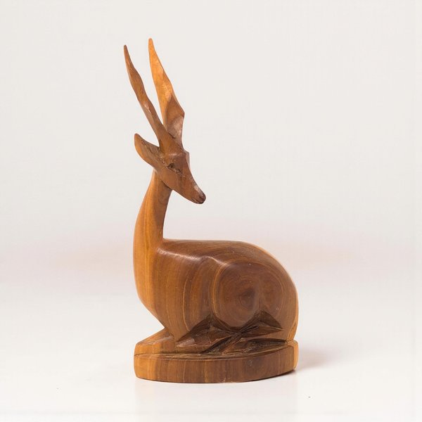 A hand-carved wooden gazelle figurine in a seated position. It features a warm, polished grain, a long slender neck, and tall pointed horns. The silhouette is smooth and stylized with minimal carved details.