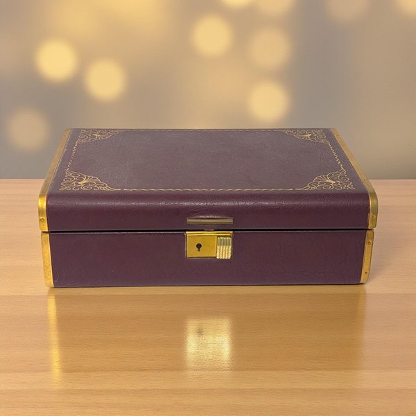 A rectangular jewelry box featuring a deep maroon exterior accented with an ornate gold filigree floral pattern. The lid is slightly domed with a metallic gold trim running along the edges.
