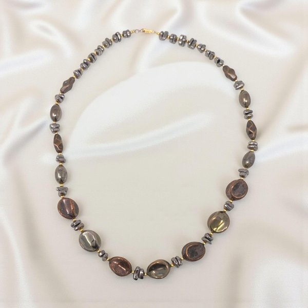 A long, single-strand necklace featuring a rhythmic alternating pattern of deep chocolate brown and matte black beads. The beads vary in shape, including smooth rounds and subtle geometric discs, creating a rich, textured appearance. .