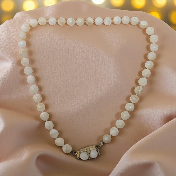 A sophisticated 16-inch necklace featuring a strand of polished, natural stone beads in earthy tones. The design centers on a distinctive front-toggling clasp in a bright gold-tone finish, which serves as both the closure and a decorative focal point. 